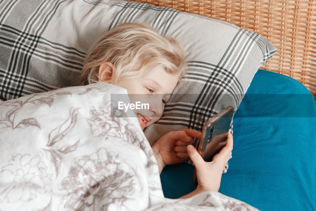 Cute girl lying in bed in morning and texting talking at social media on smartphone cellphone. 