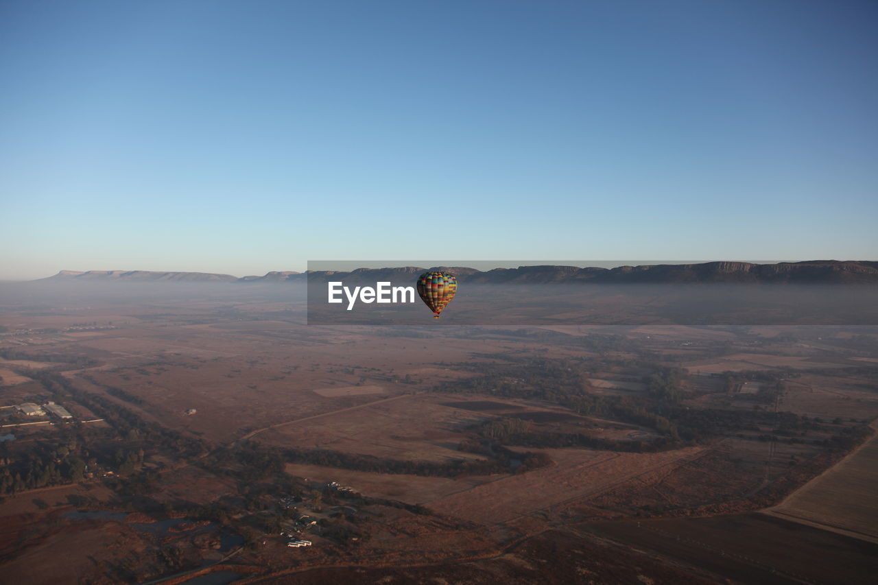 Hot air balloon flying over landscape against clear blue sky