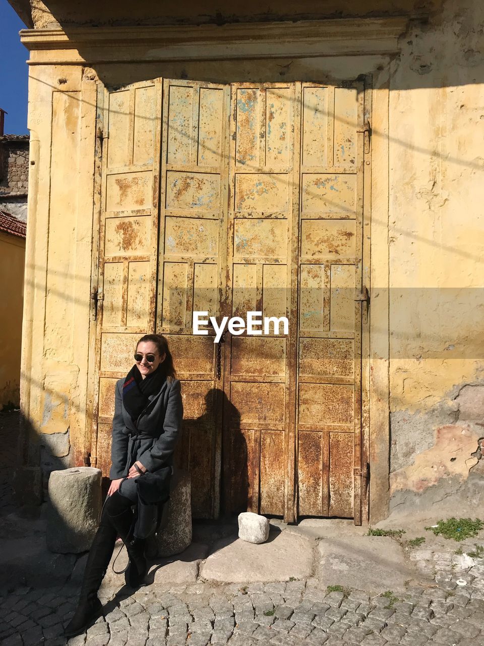 Young woman wearing sunglasses while sitting against old door