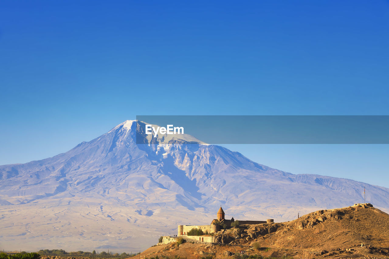 Scenic view of built structure against snowcapped mountain and sky