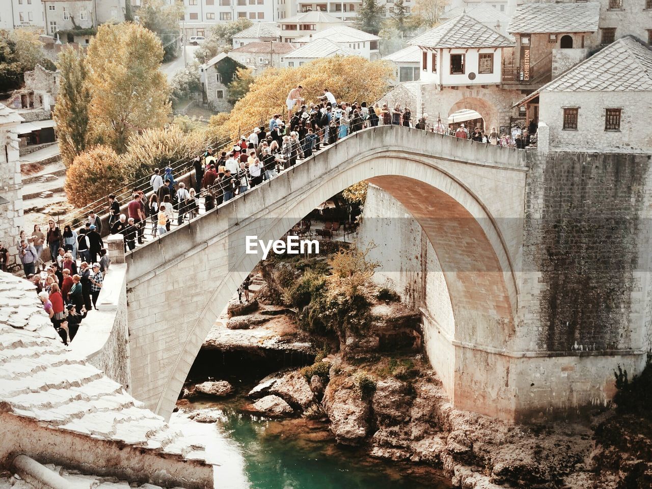 PEOPLE AT RIVERBANK AGAINST BUILDINGS