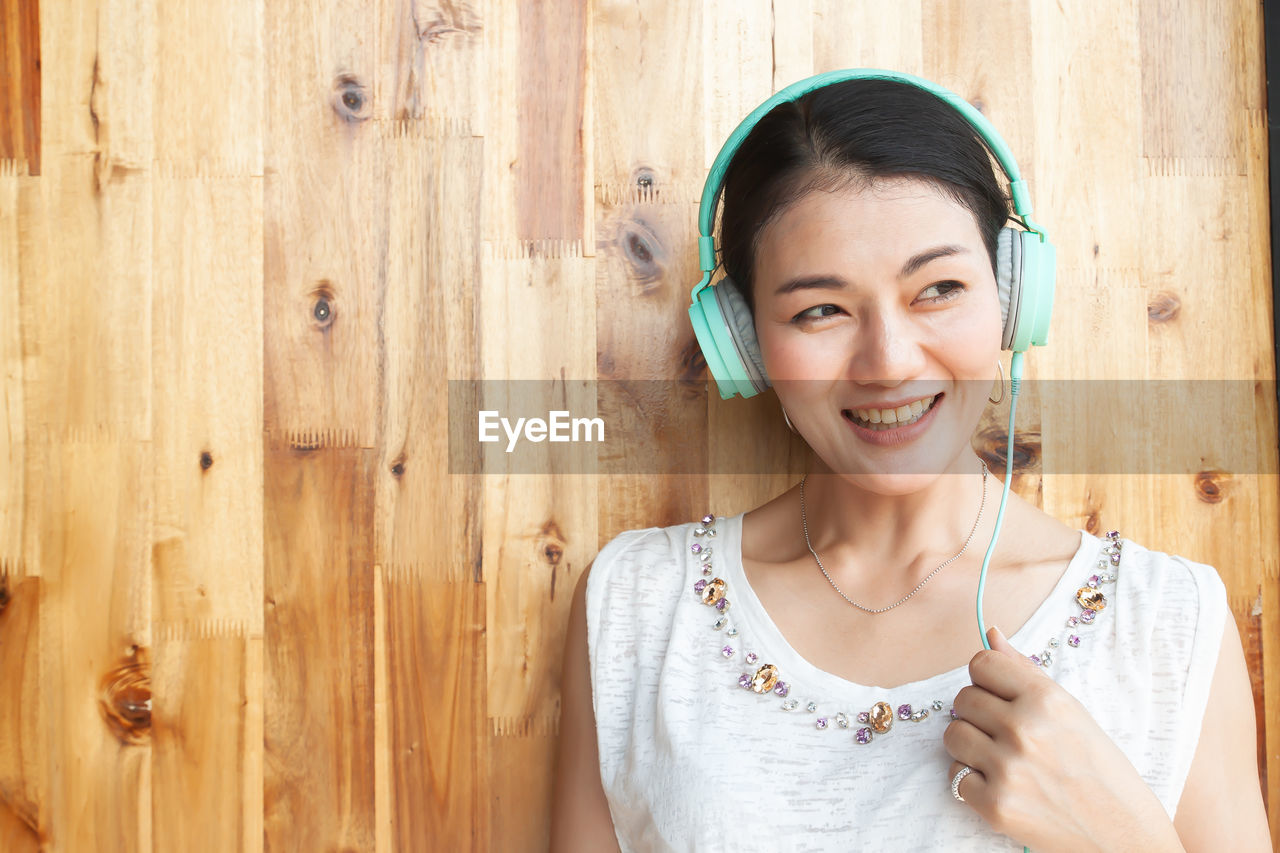 Close-up of happy woman looking away while wearing headphones against wall