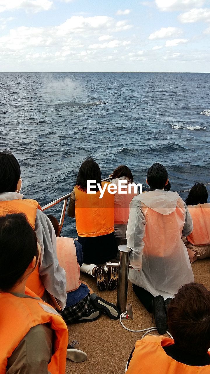 Rear view of people sitting on boat sailing in sea against sky