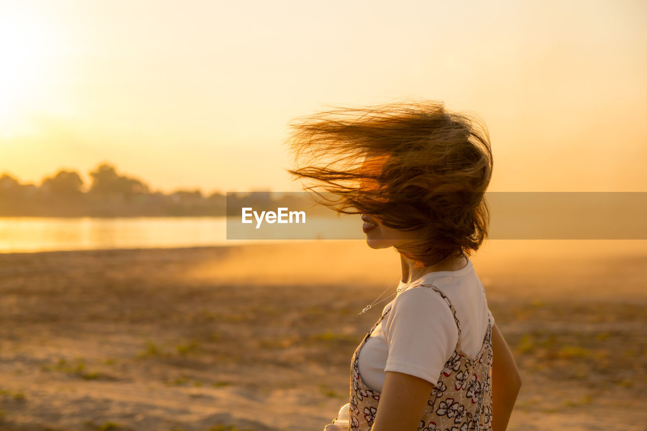 Woman with tousled hair standing against lake