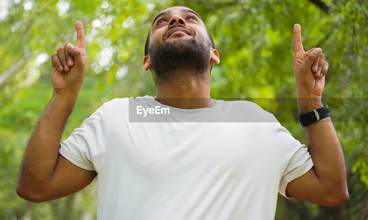 one person, adult, men, arm, waist up, human limb, limb, nature, casual clothing, person, t-shirt, lifestyles, plant, arms raised, gesturing, sports, green, relaxation, young adult, happiness, outdoors, emotion, beard, summer, hand, positive emotion, standing, spirituality, looking, portrait, exercising, day, facial hair, leisure activity, tree, cheerful, smiling, enjoyment, muscular build