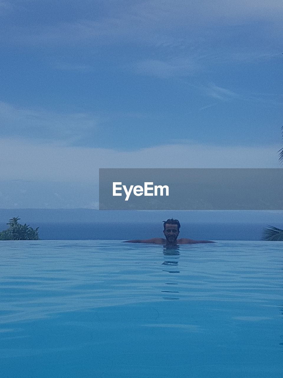 PORTRAIT OF YOUNG MAN SWIMMING IN POOL AGAINST SKY