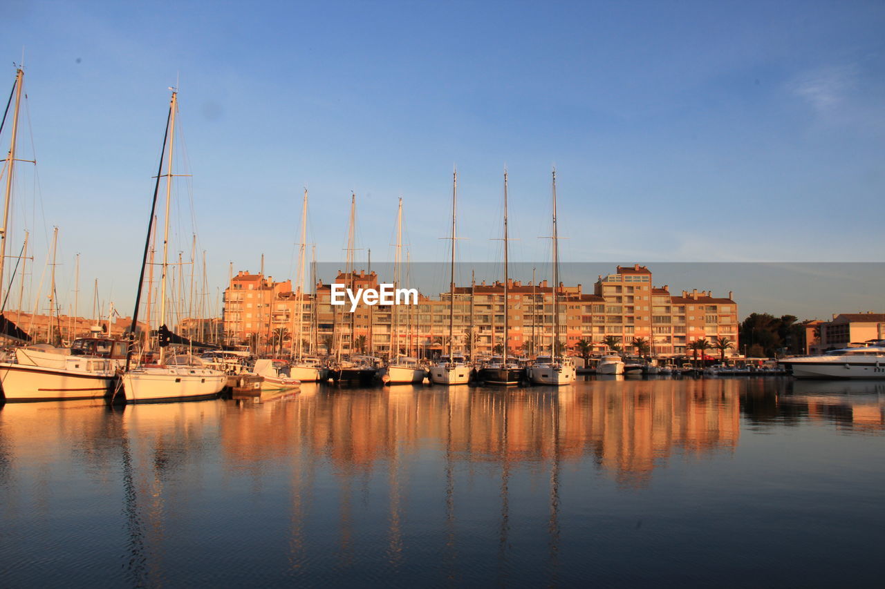 Sailboats moored in harbor by buildings against sky