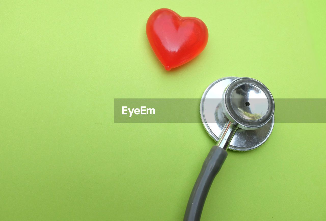 Close up red heart white stethoscope on green doctor table.health concept