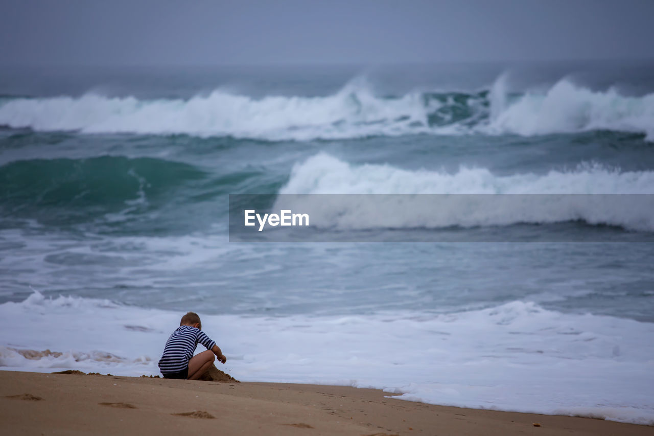 Kid plays on shore of huge, raging ocean. childhood freedom and adventure. discovery of the world