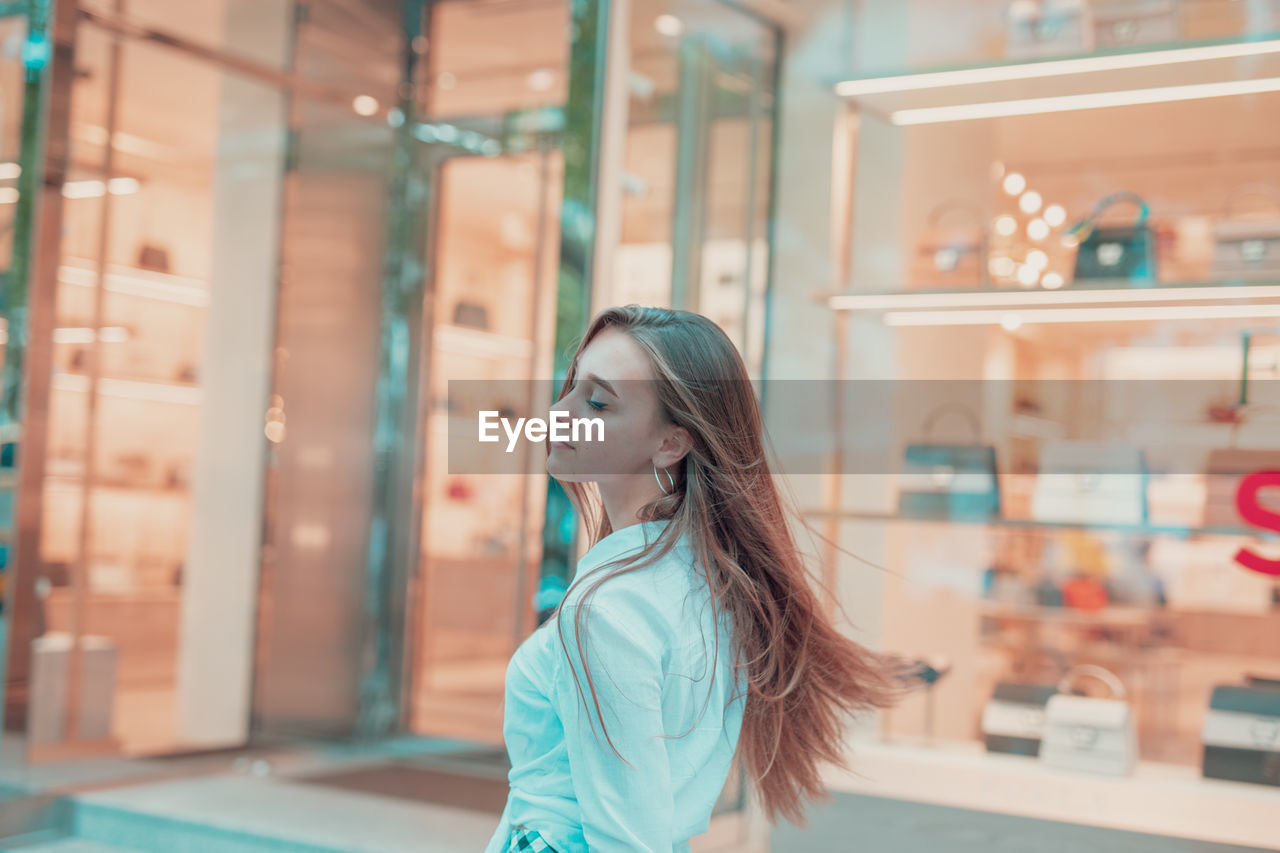 Young woman with eyes closed standing in store window