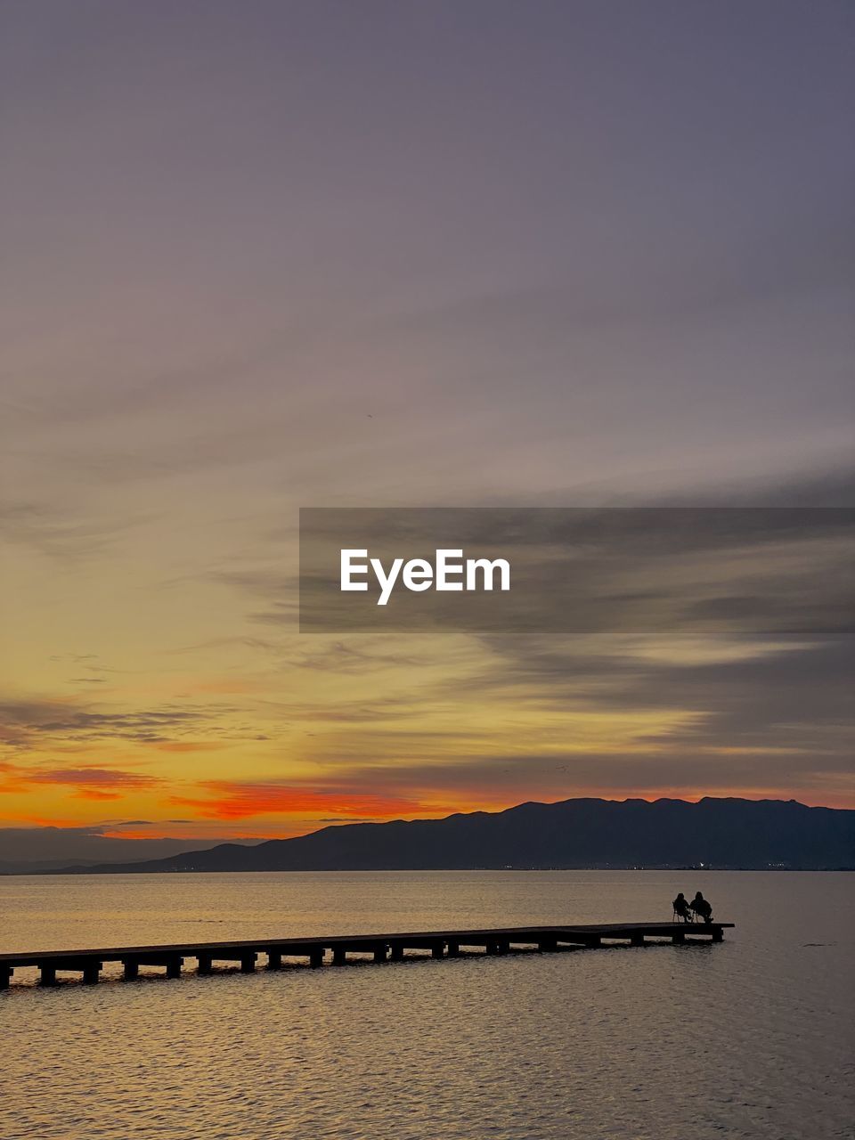 Scenic view of couple on pier on lake against sky during sunset