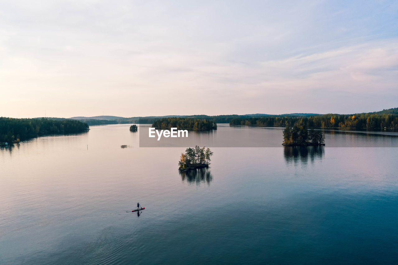 Aerial view of lakes, islands, forest and a person paddle boarding 