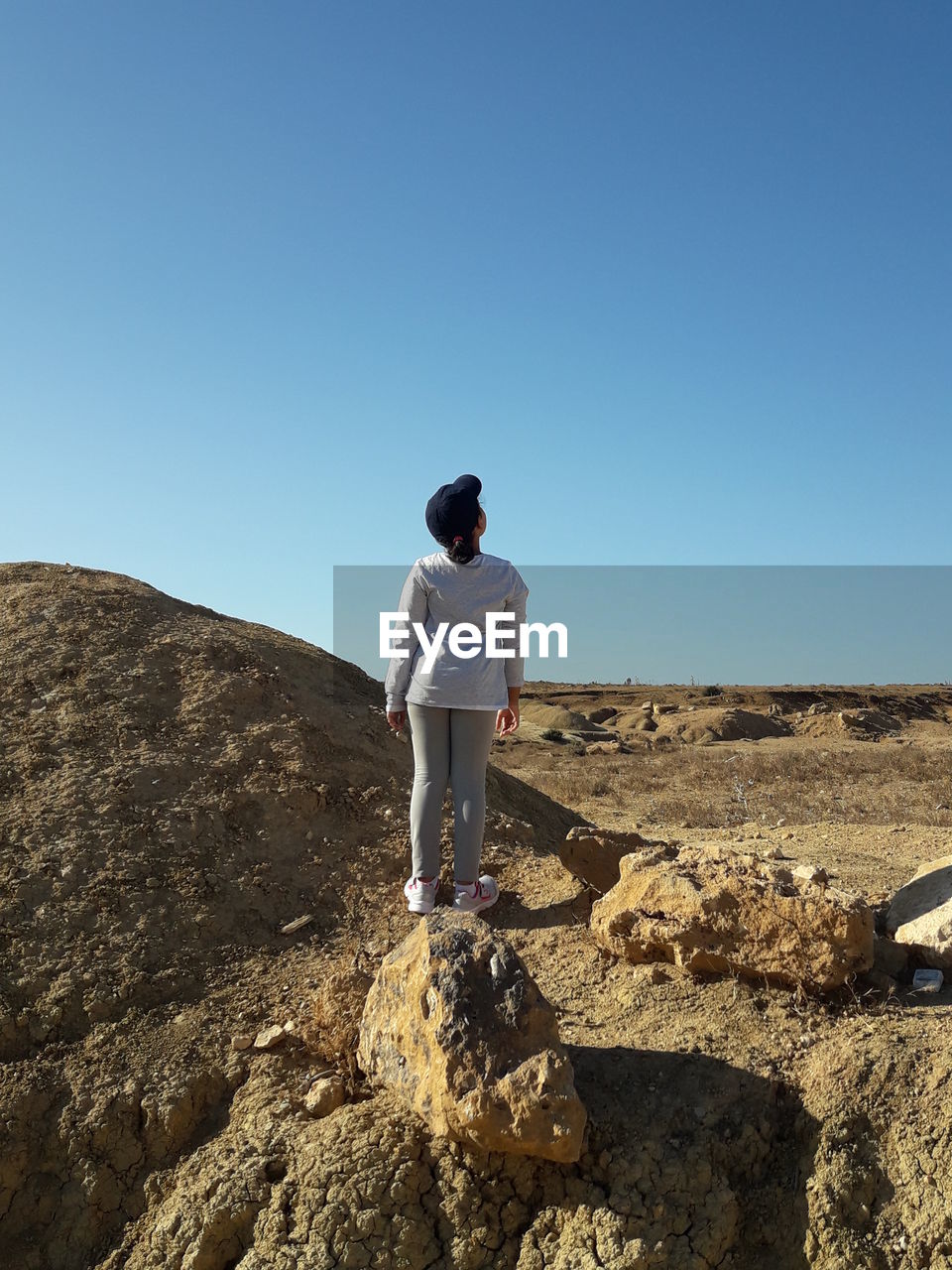 Rear view of girl standing on rock against clear blue sky