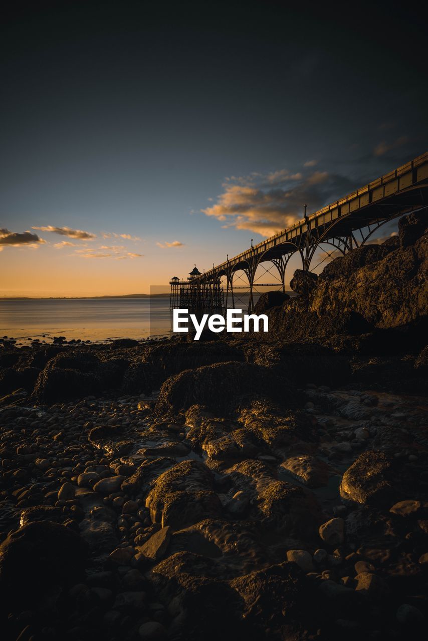 Rocks by bridge against sky during sunset