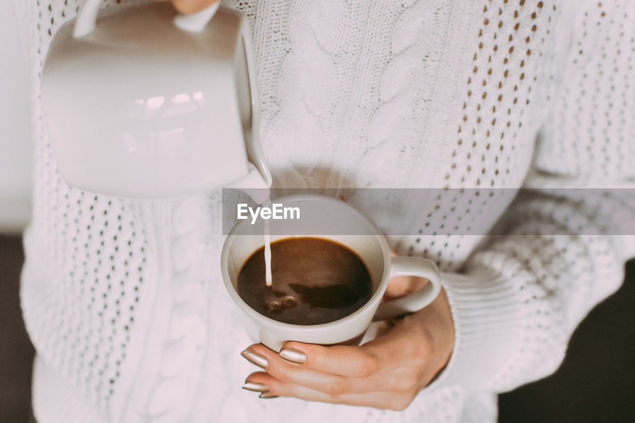 Midsection of woman pouring milk in coffee