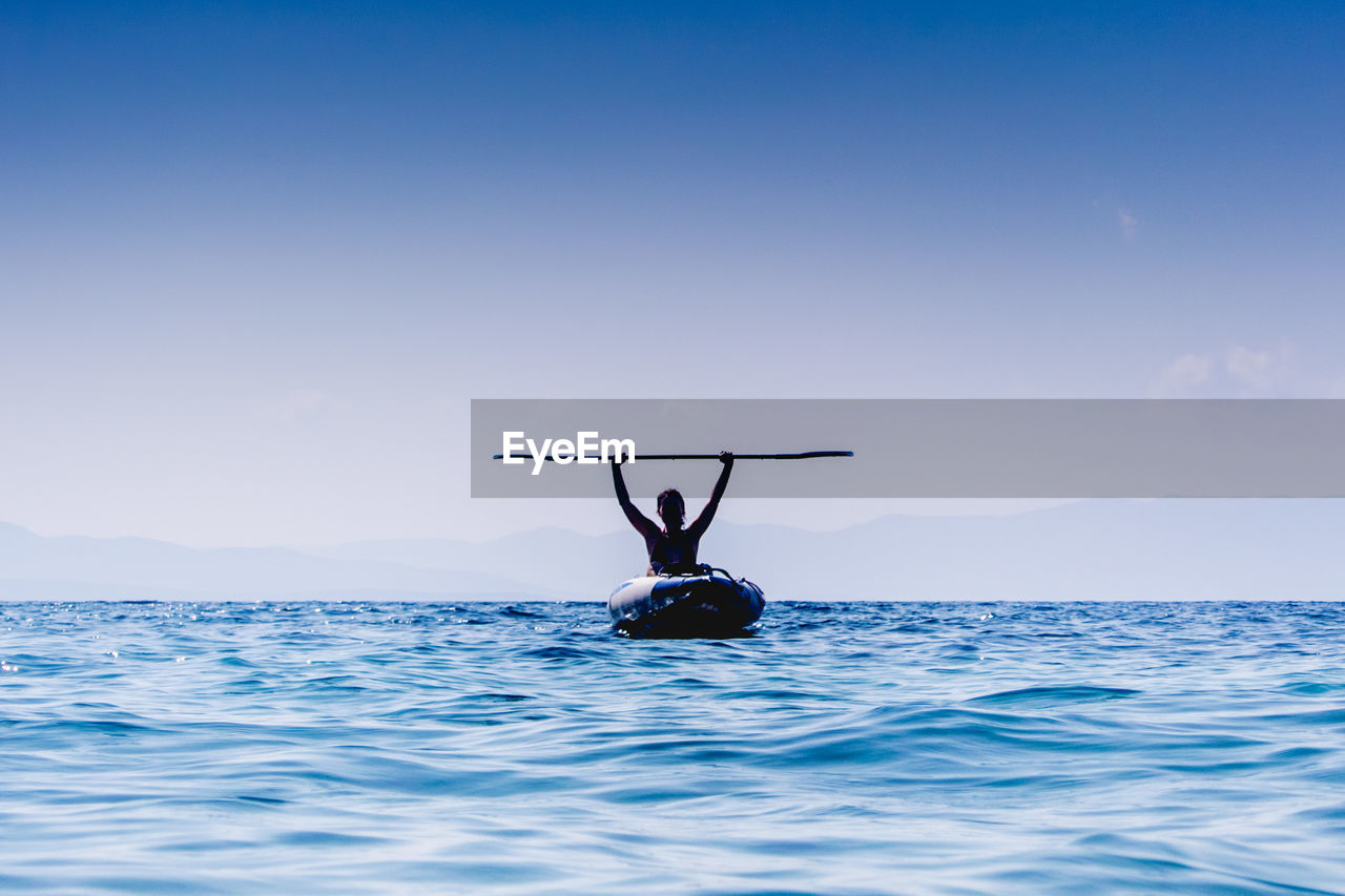 Woman holding oar moving in boat on sea against sky