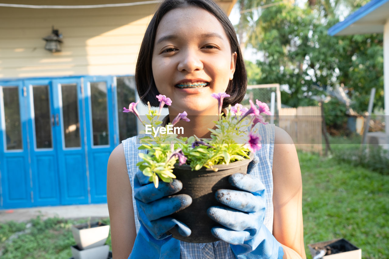 Portrait of smiling woman holding potted plant while standing in yard