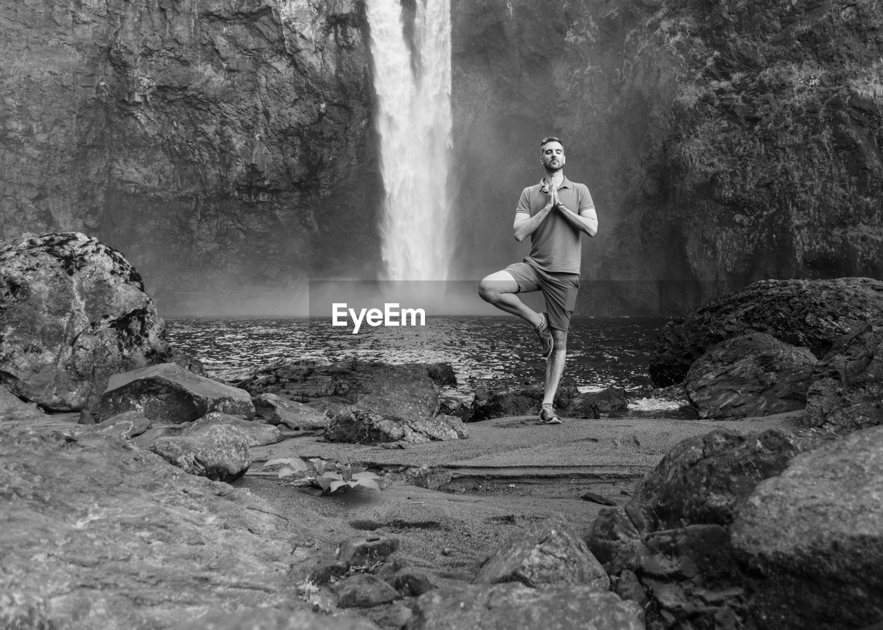 Full length of man meditating while standing against waterfall