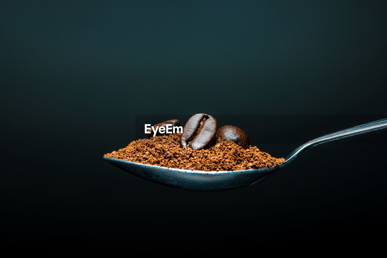Roasted coffee beans and ground coffee on a spoon isolated on black background