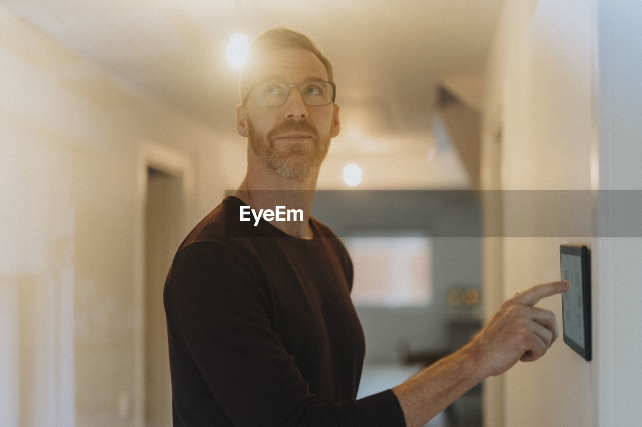 Mature man adjusting room lights through digital tablet while standing at smart home