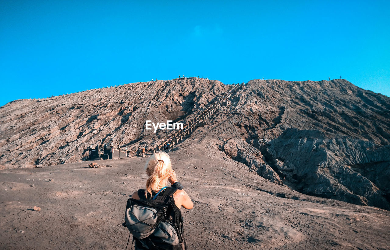 Rear view of woman standing on land against mountain and sky