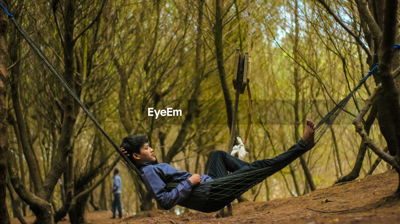 Man lying in hammock amidst trees in forest