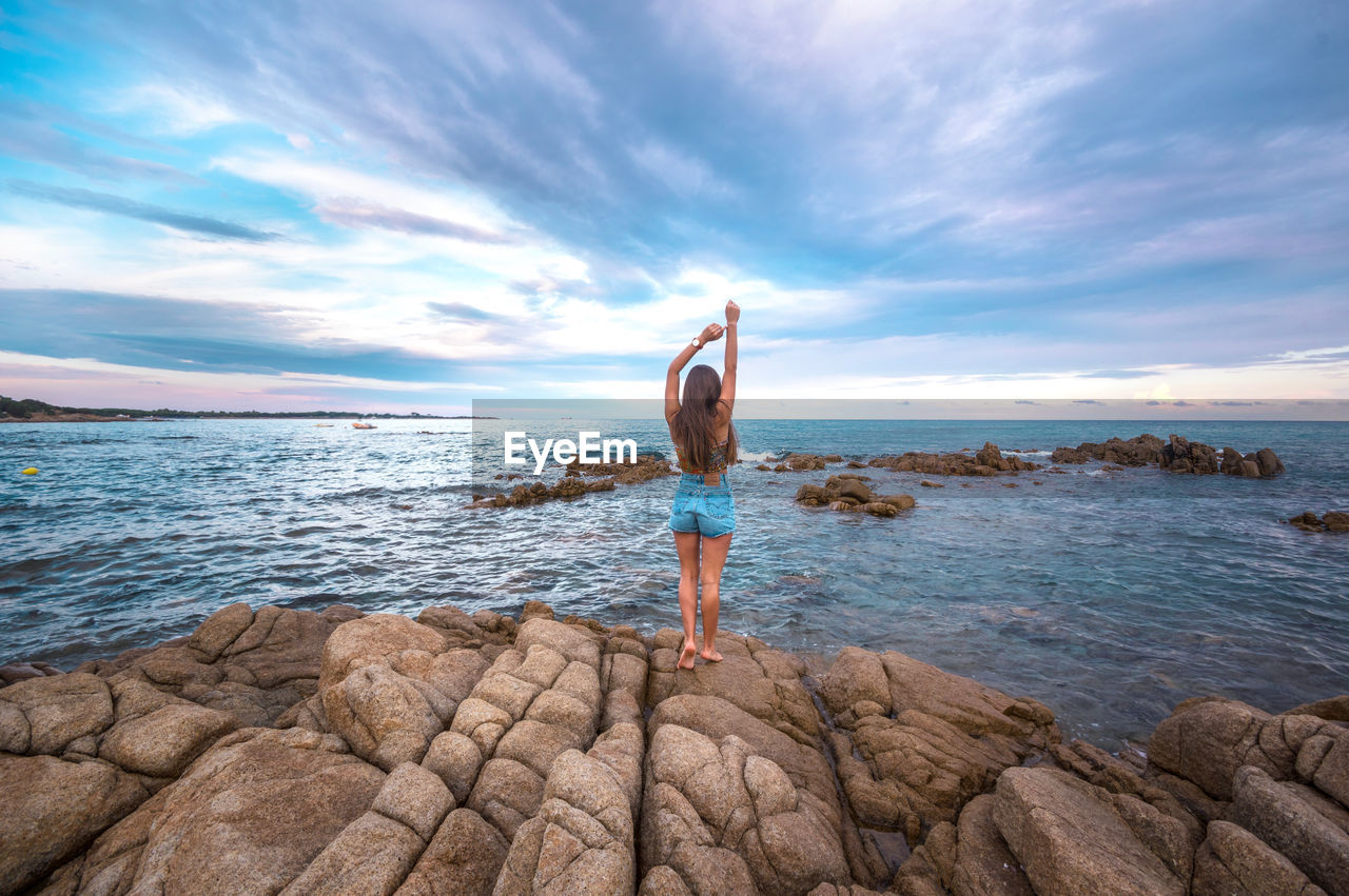 Rear view of person standing on rock by sea against sky