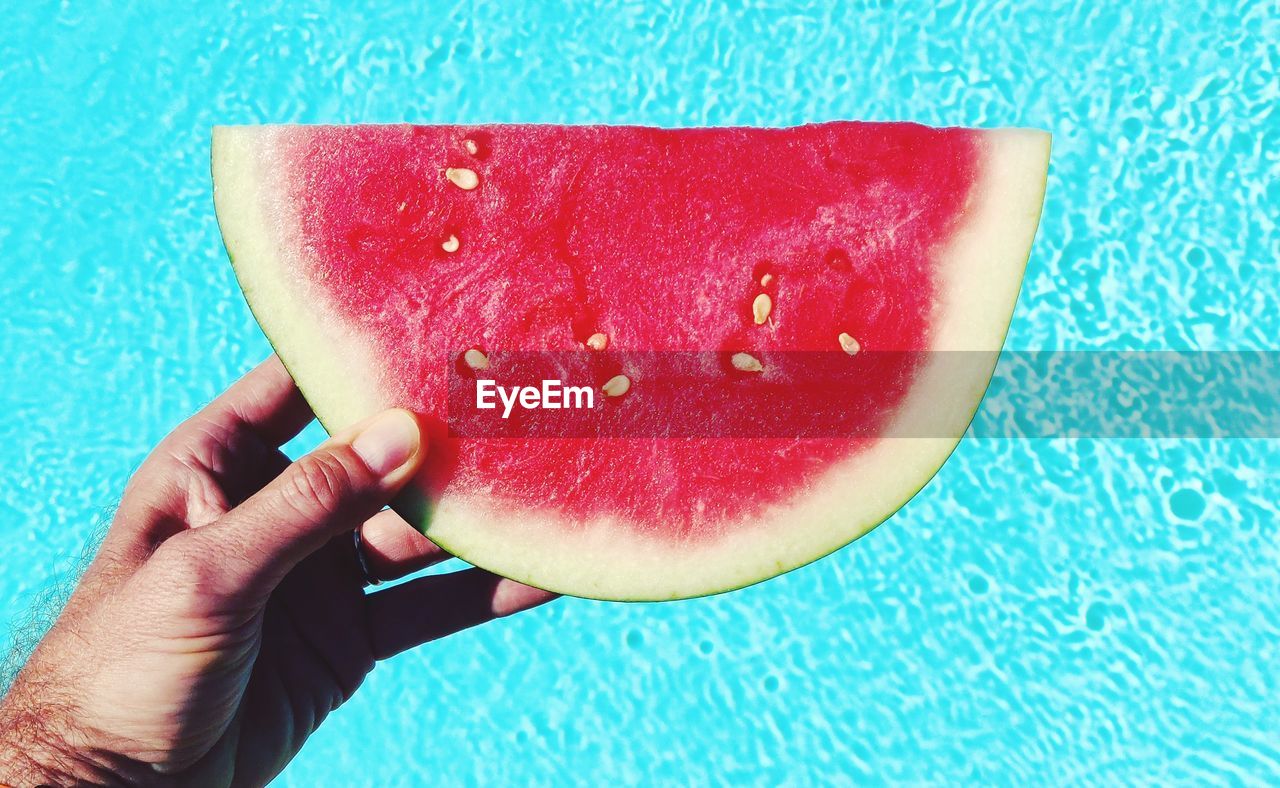 Close-up of hand holding watermelon against swimming pool