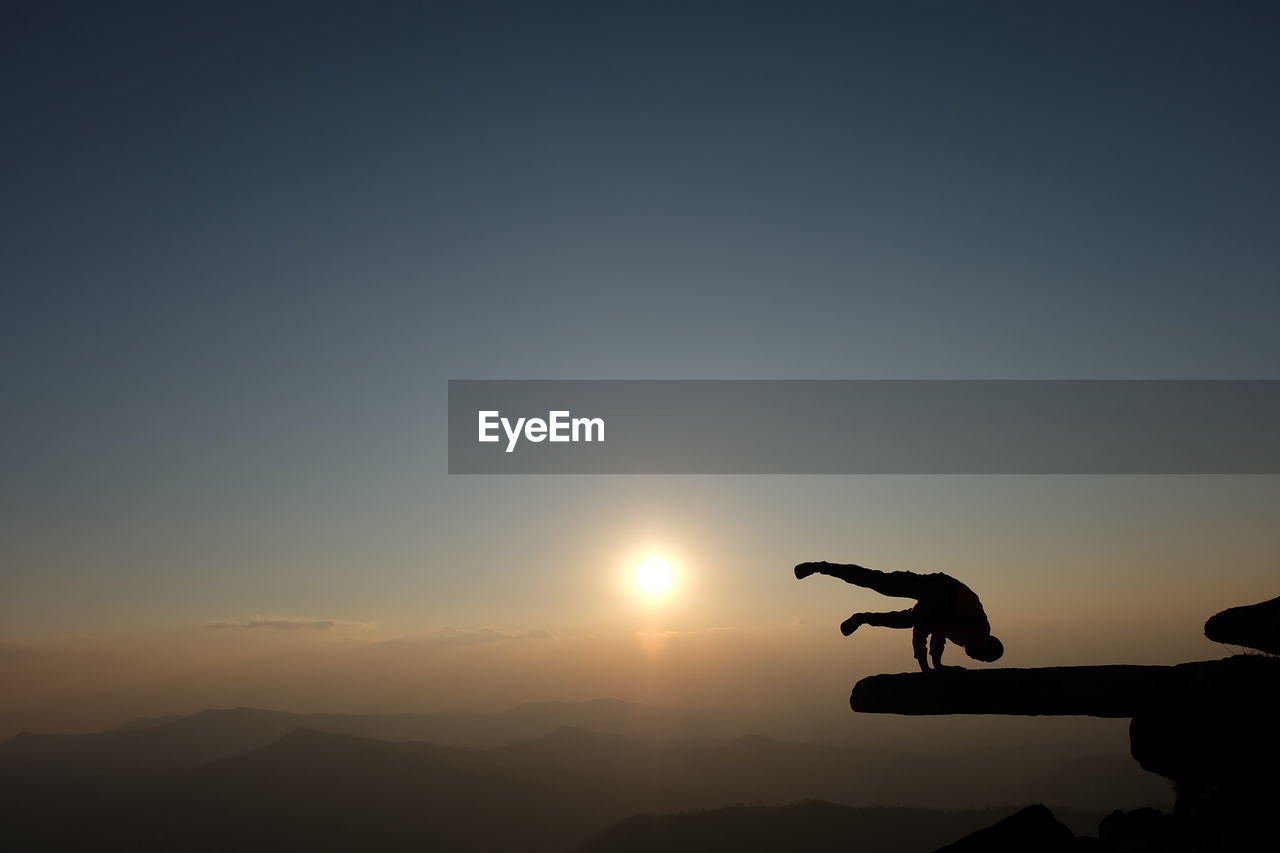 Silhouette man doing handstand on mountain against sky during sunset