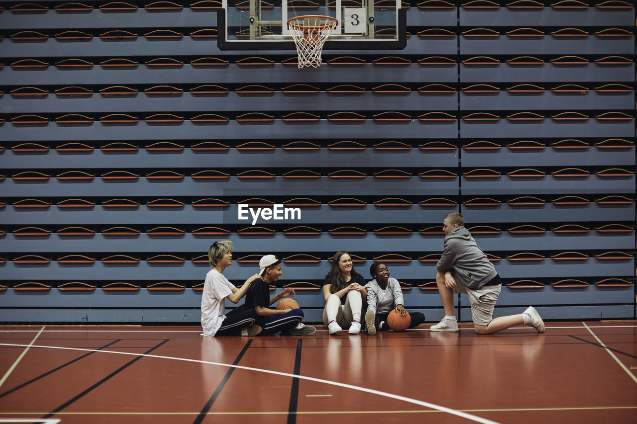 Smiling boys and girls talking with each other at basketball court in school