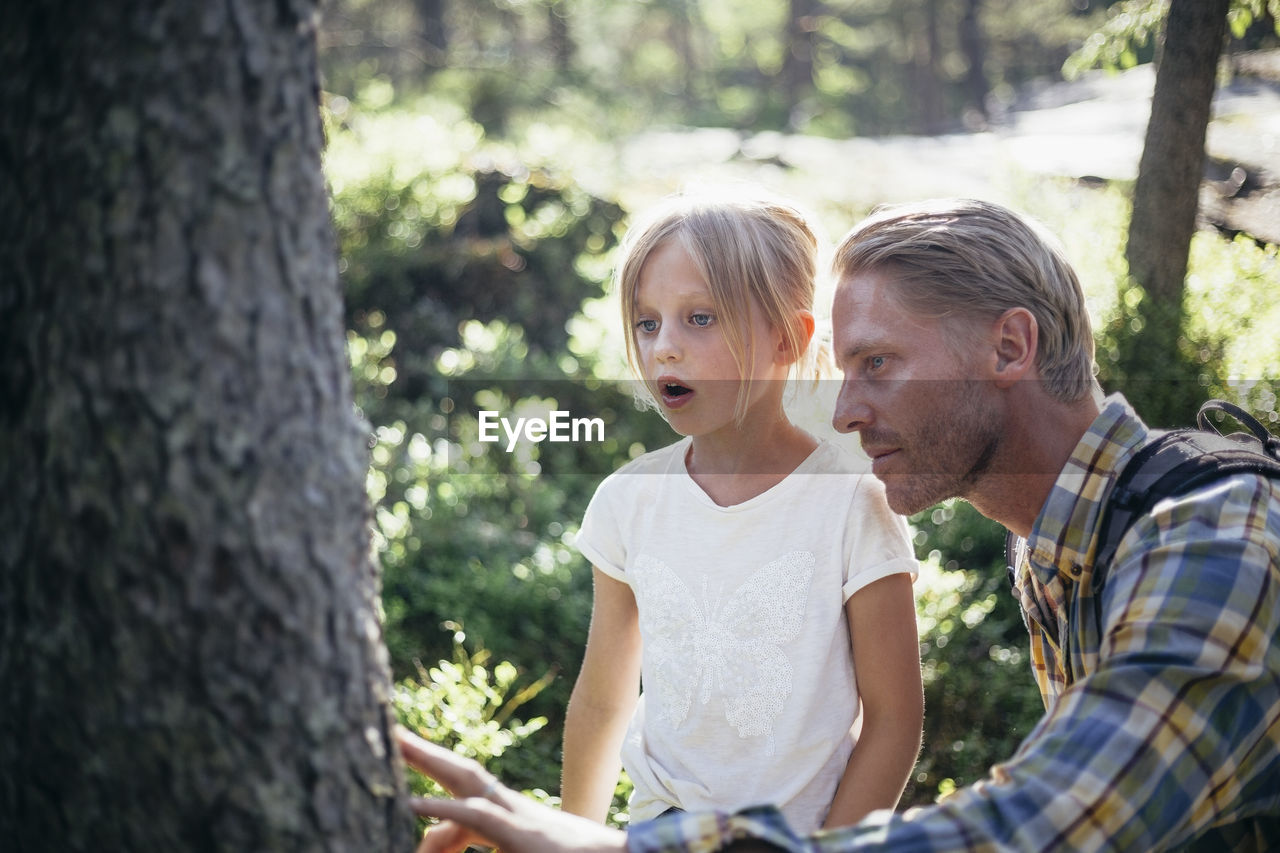 Father and daughter looking at tree trunk in forest