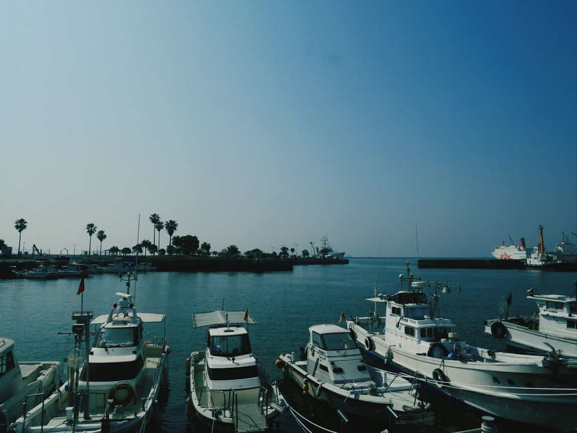 Boats moored on sea against clear blue sky