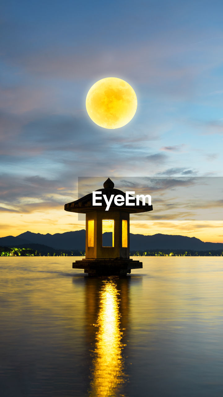 Built structure in lake against sky during sunset