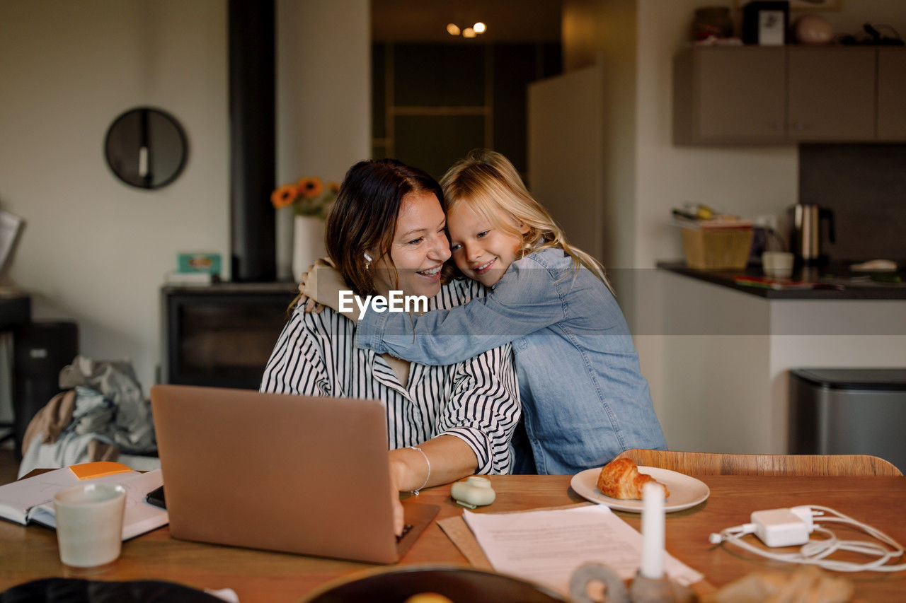 Boy embracing mother working on laptop at home