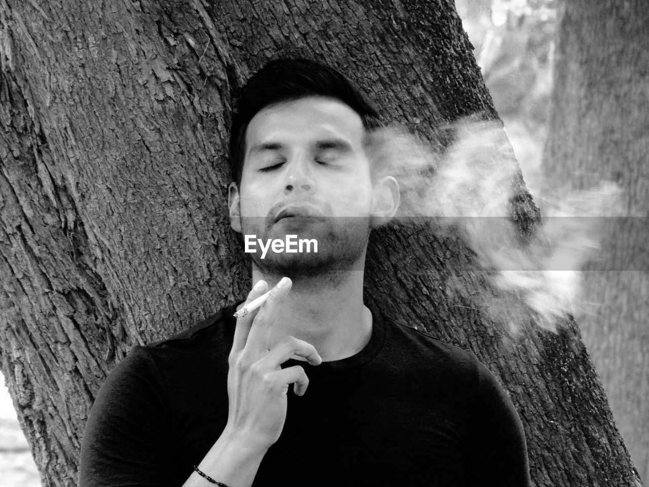 Young man smoking by tree trunk