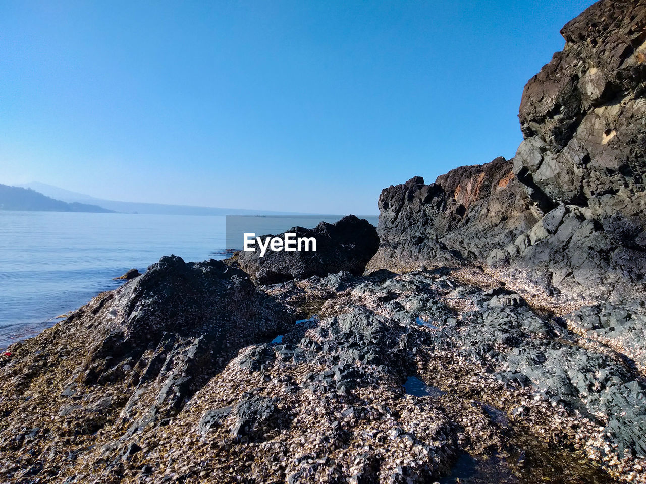 ROCK FORMATION ON SEA AGAINST CLEAR BLUE SKY