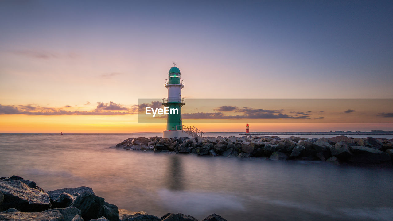 Lighthouse by sea against sky during sunset