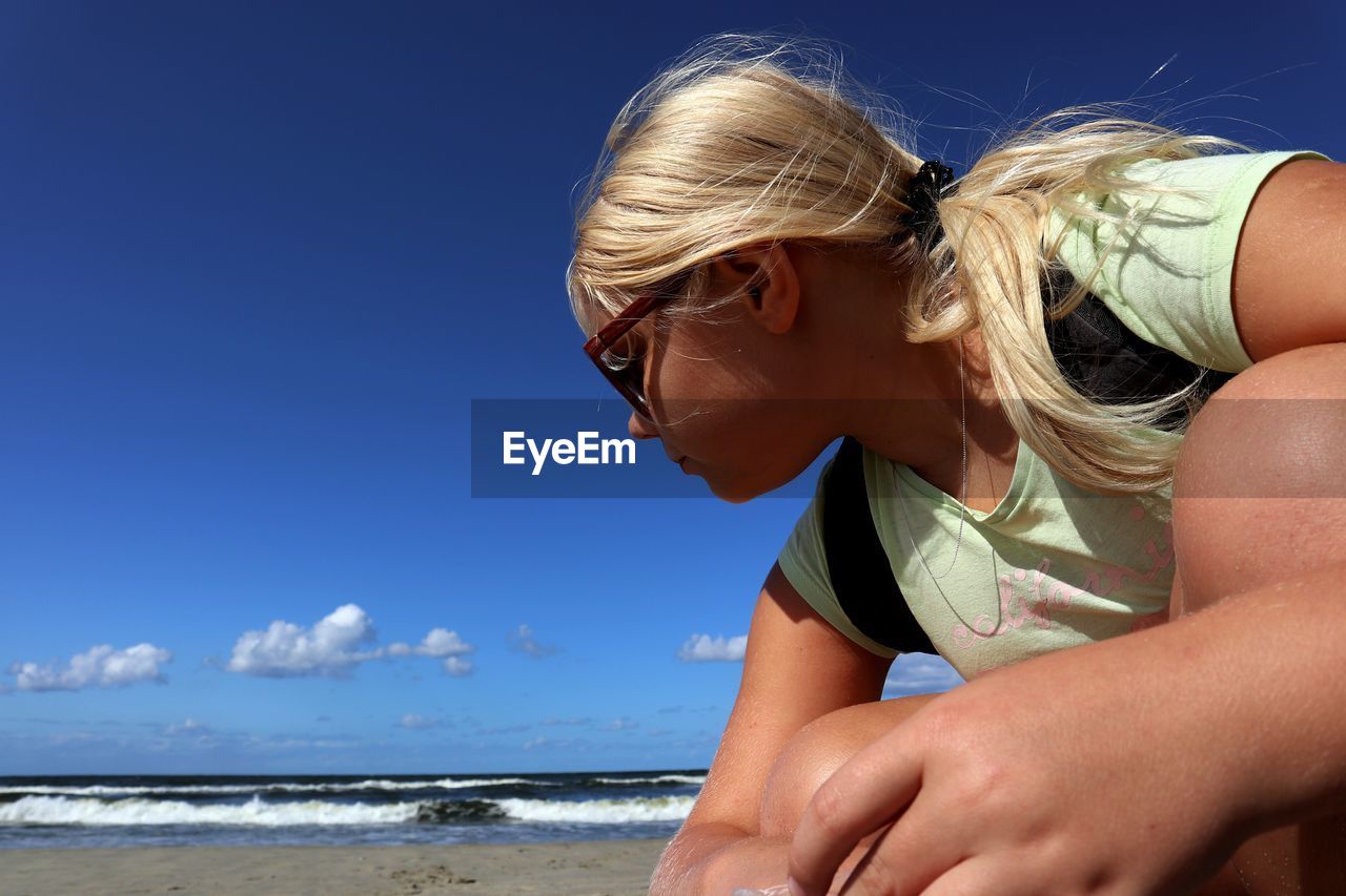 Girl crouching at beach against blue sky