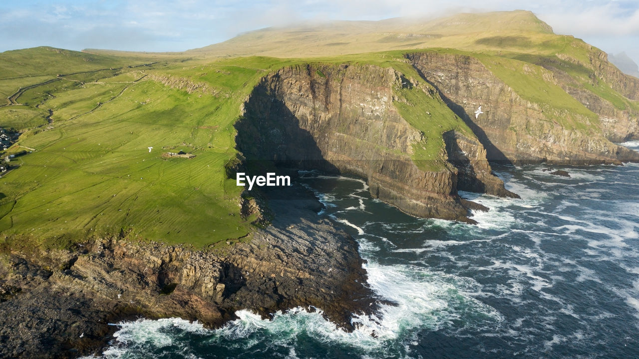 Scenic view of cliff by sea against cloudy sky