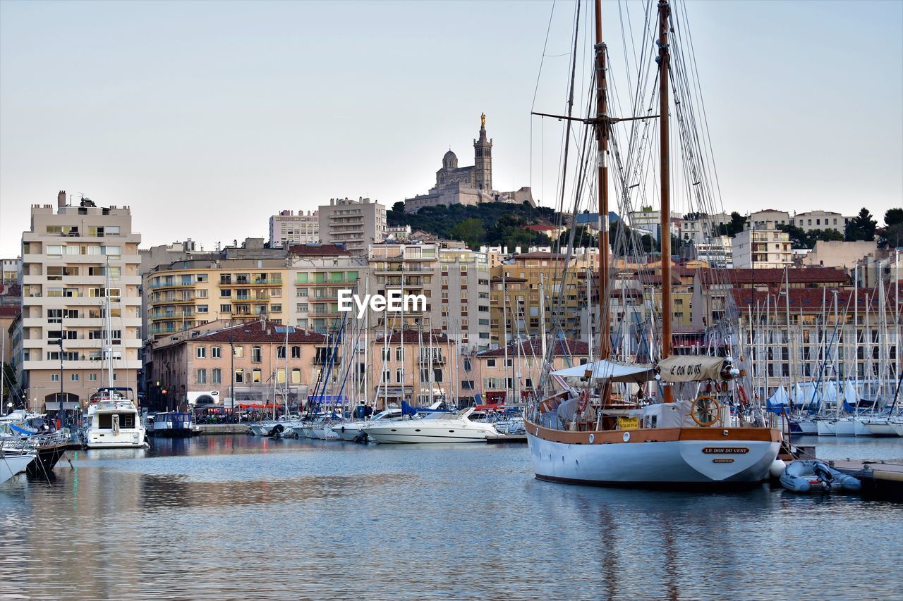 SAILBOATS MOORED ON HARBOR BY BUILDINGS AGAINST SKY