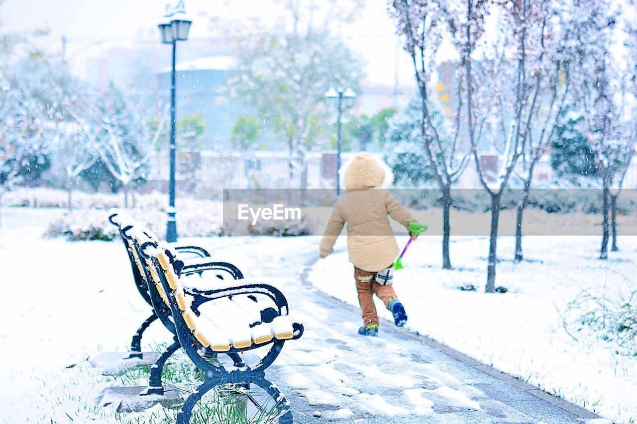 Rear view of child walking by bench on footpath during winter