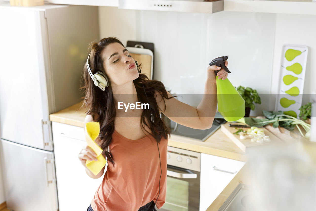 Young woman in kitchen cleaning and listening to music