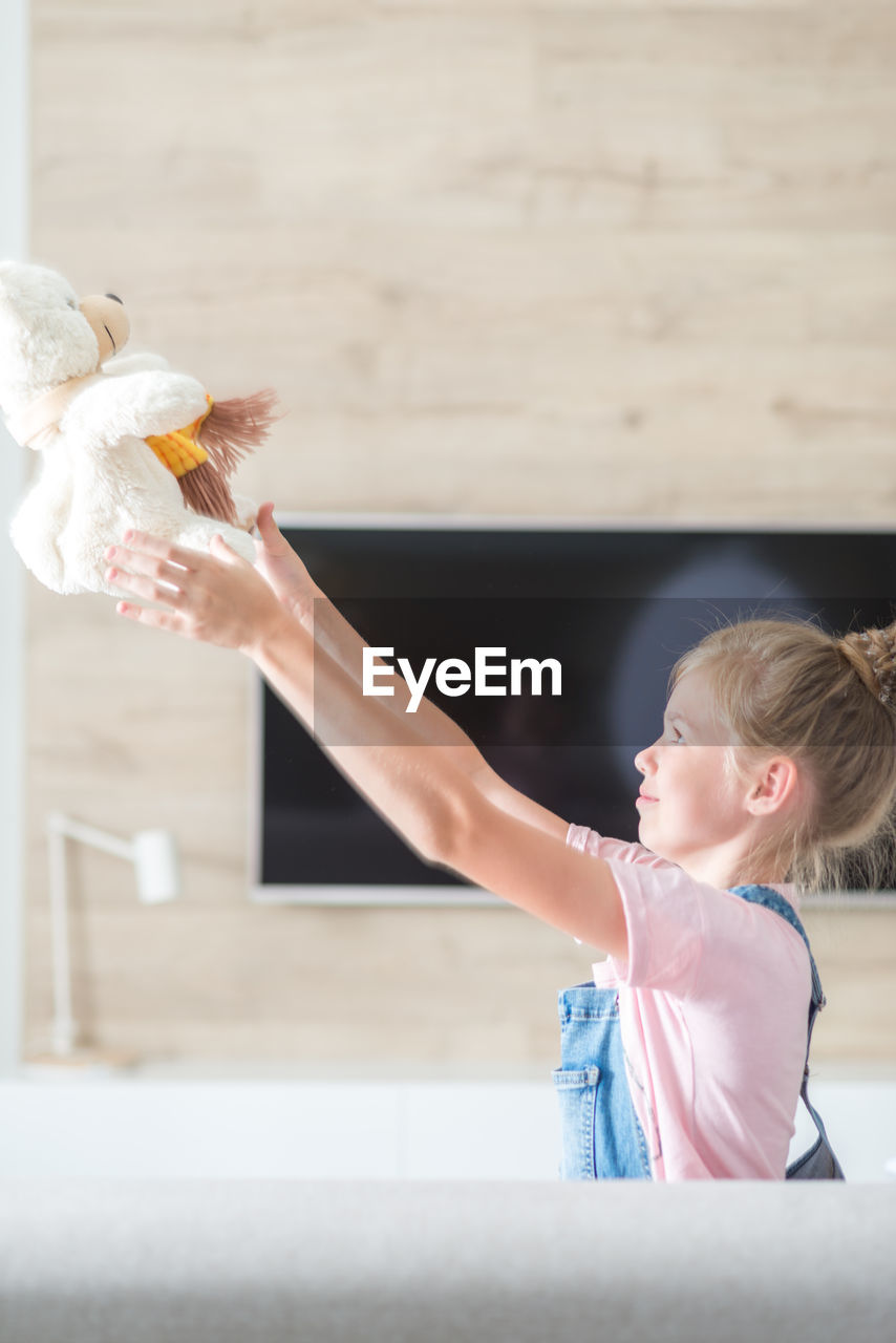 Side view of girl playing with teddy bear at home