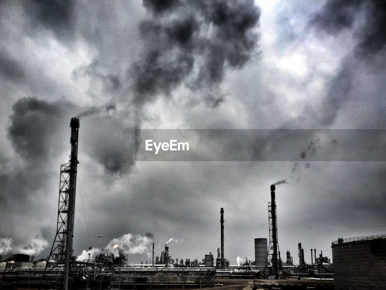 Smoke stacks at factory against cloudy sky