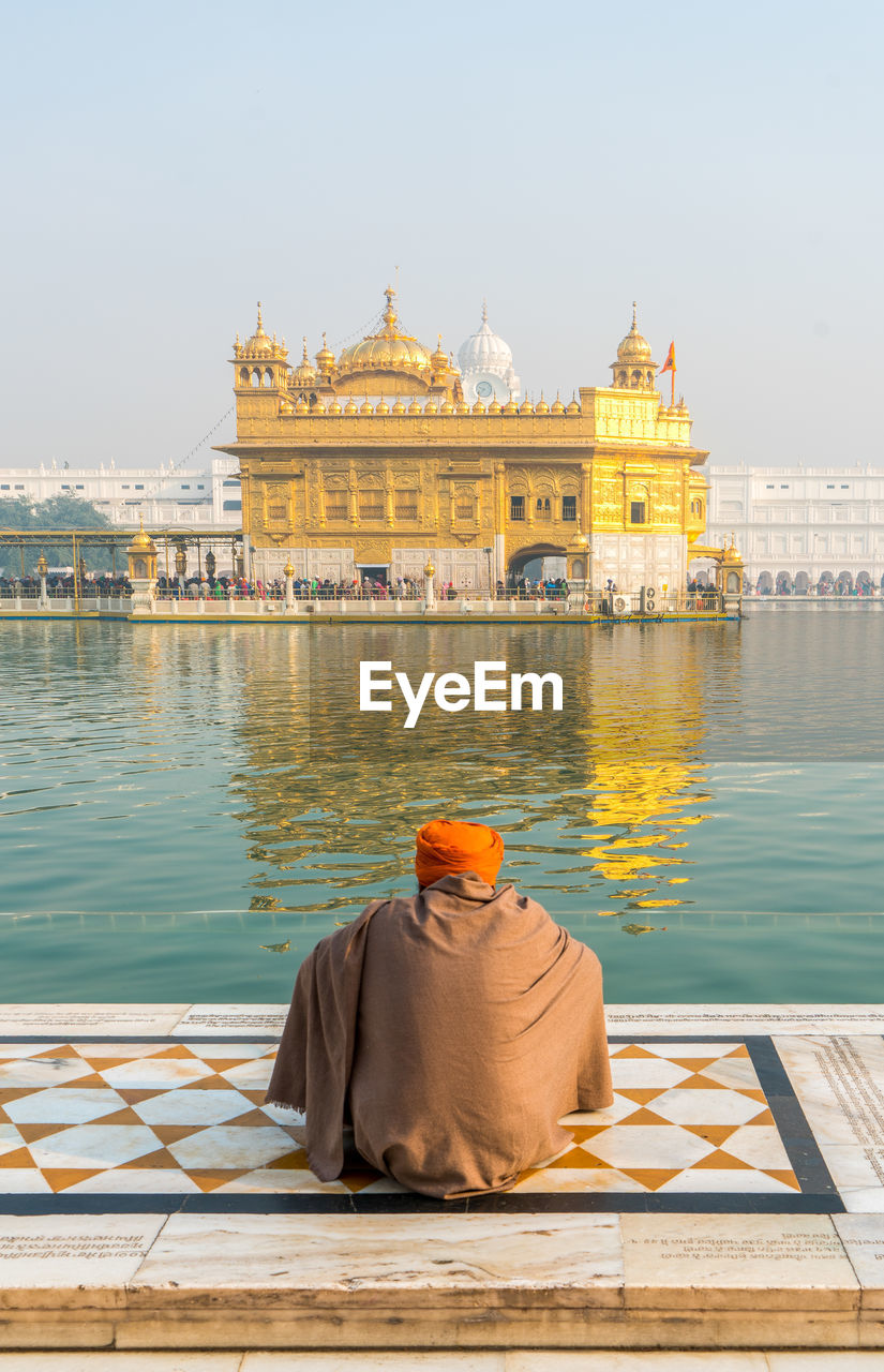 Rear view of man praying against golden temple amidst standing water