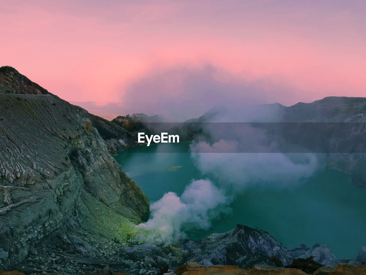 Smoke by crater lake against sky during sunset