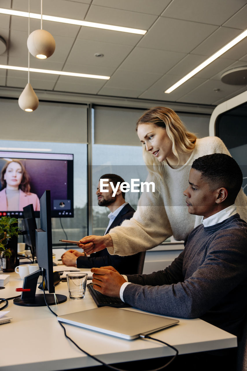 Businesswoman assisting male colleague over computer at desk in coworking office