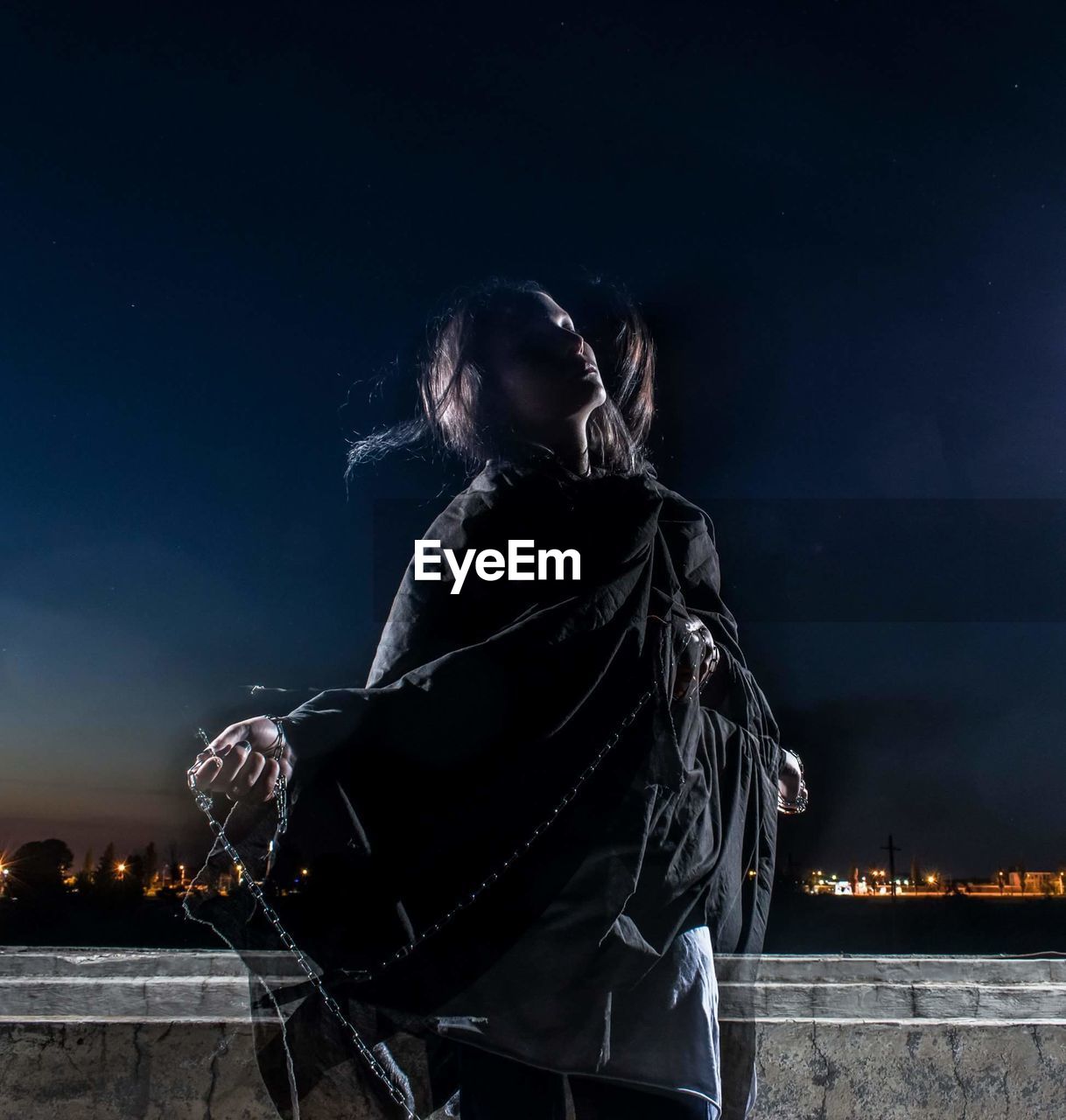 Double exposure image of woman holding chain against sky at night