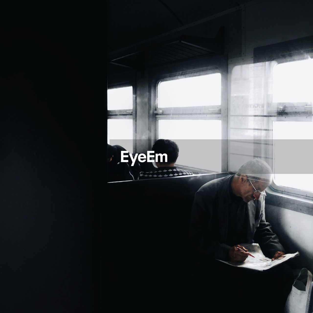 Mature man reading newspaper while sitting by window in train