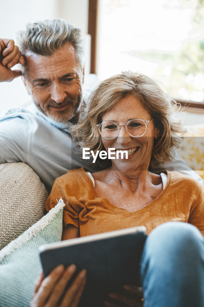 Happy woman wearing eyeglasses using tablet pc with man at home